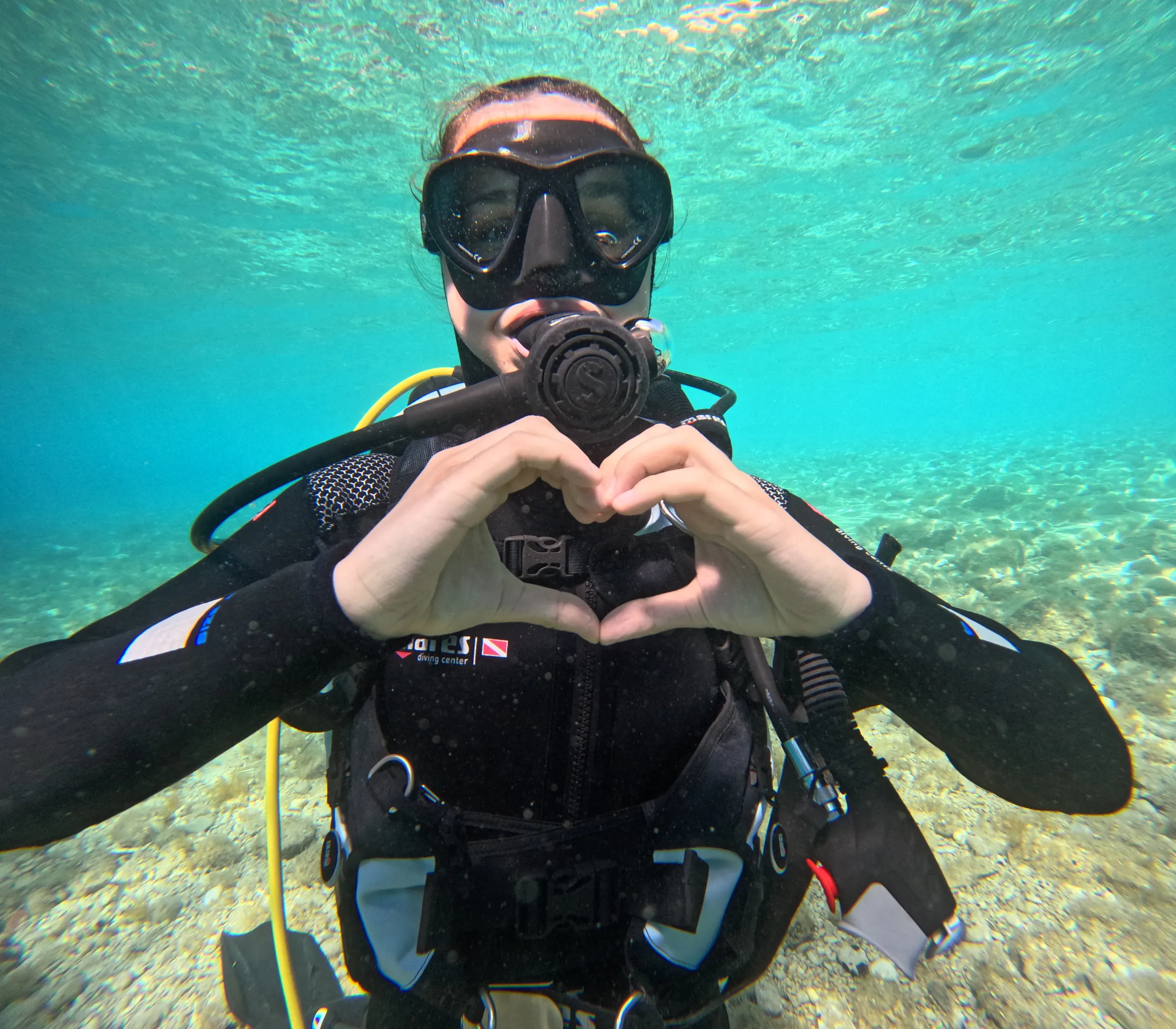 Diver making a heart with her hands underwater in clear shallow water